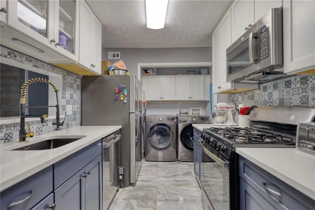Kitchen featuring stainless steel appliances, tasteful backsplash, washing machine and dryer, a textured ceiling, and light stone counters