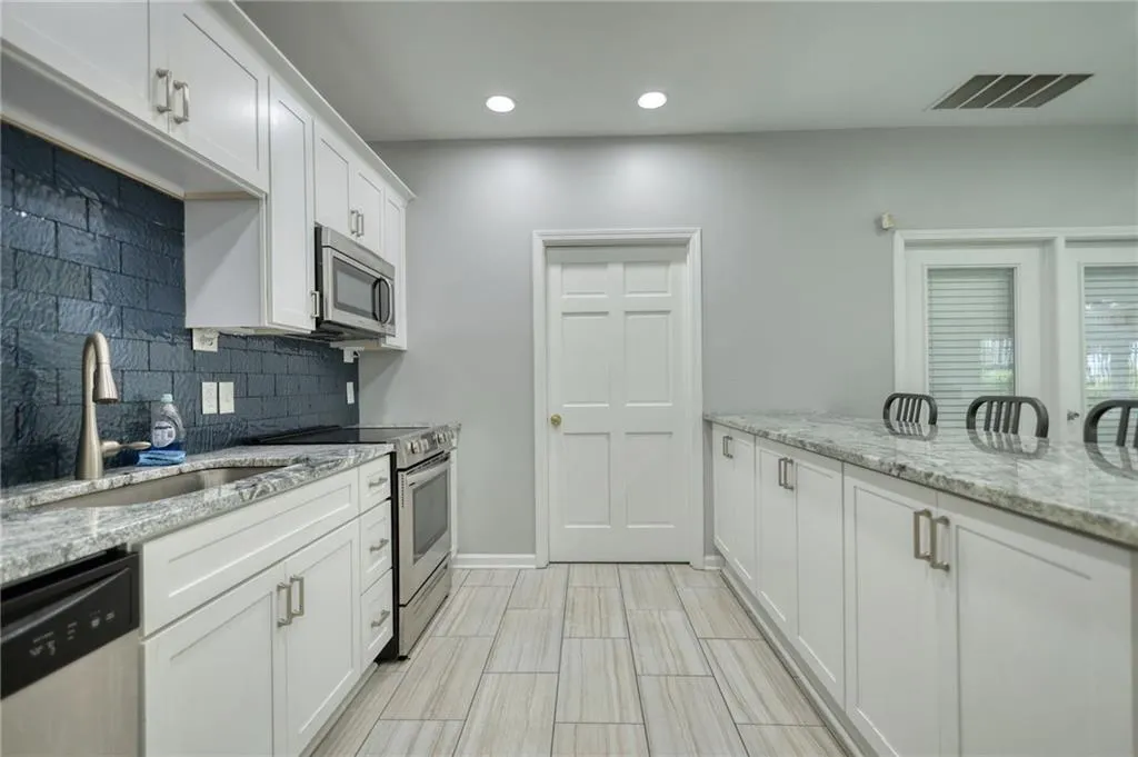 Kitchen featuring light stone countertops, white cabinets, stainless steel appliances, recessed lighting, and decorative backsplash