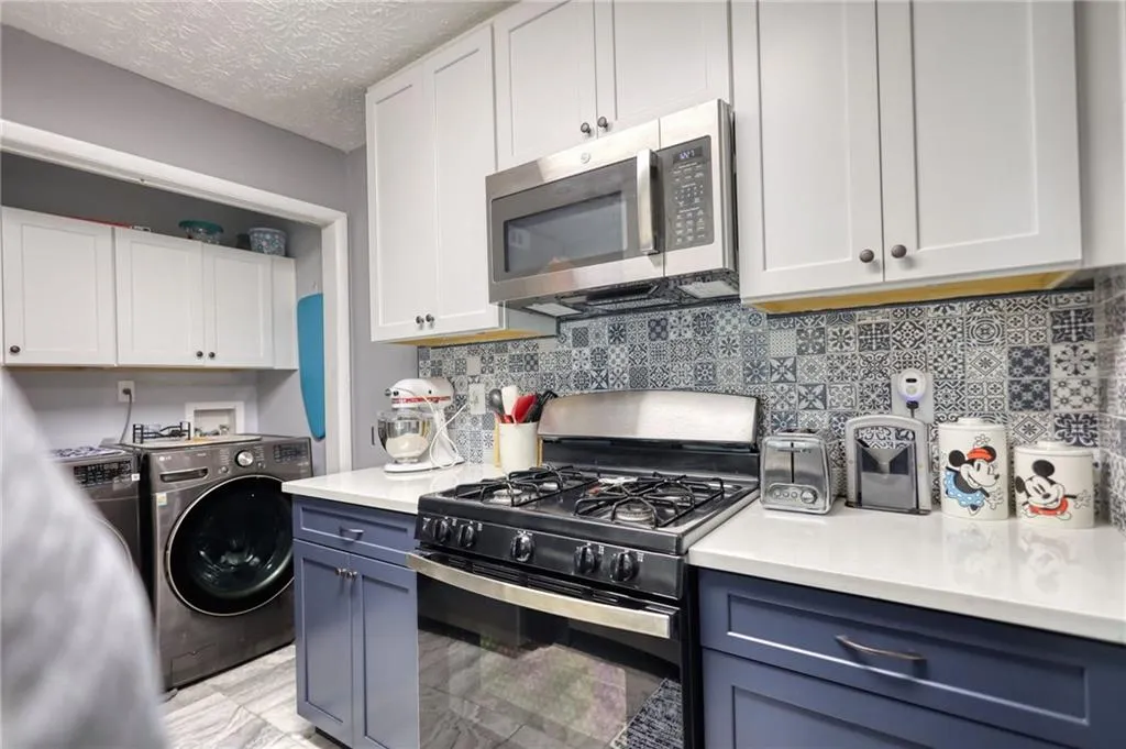Kitchen with black range with gas cooktop, white cabinets, stainless steel microwave, and a textured ceiling