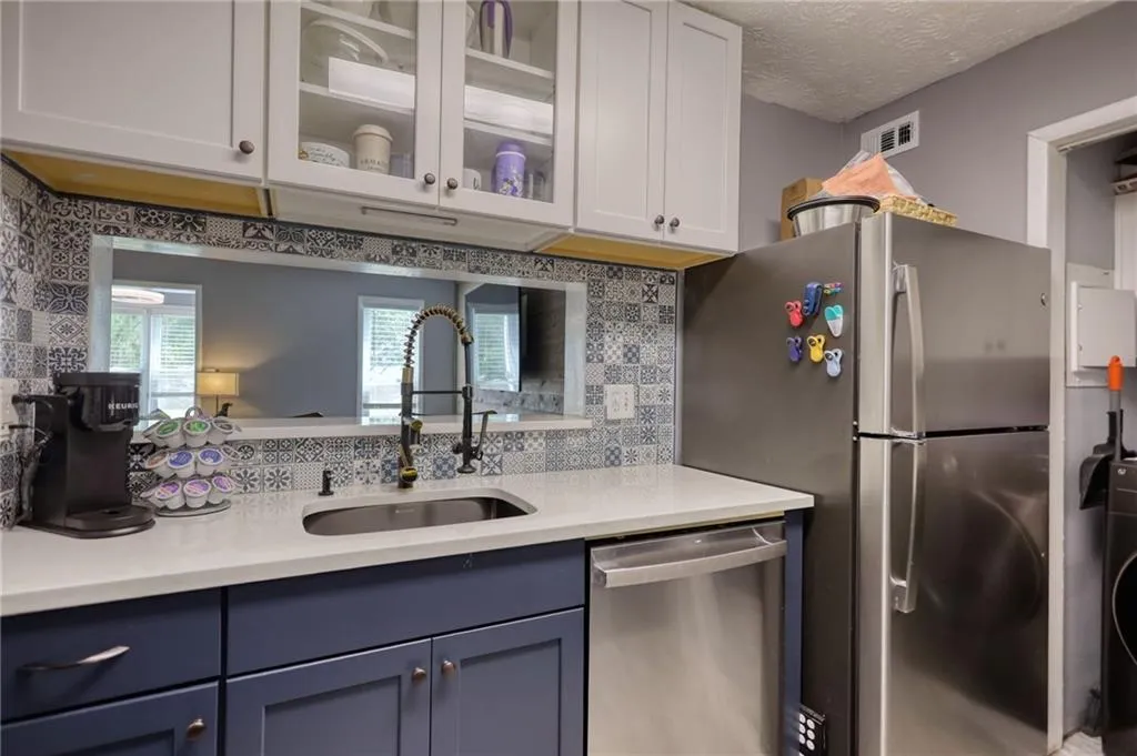Kitchen featuring appliances with stainless steel finishes, glass insert cabinets, light stone countertops, tasteful backsplash, and a textured ceiling