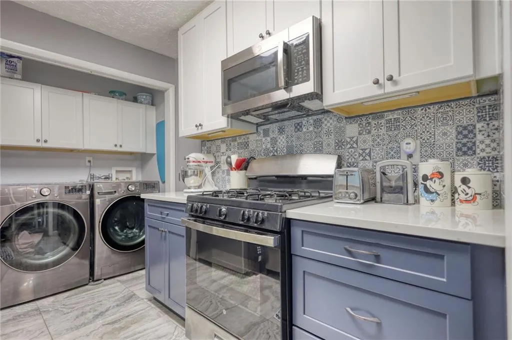 Kitchen with appliances with stainless steel finishes, white cabinetry, decorative backsplash, washing machine and dryer, and a textured ceiling