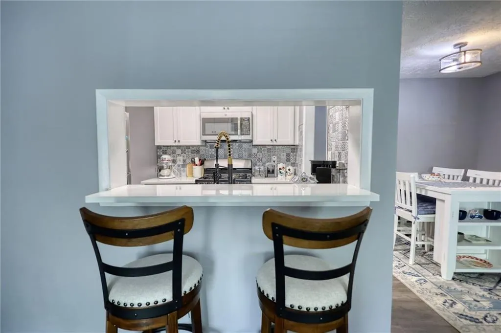 Kitchen featuring a kitchen breakfast bar, white cabinetry, stainless steel appliances, tasteful backsplash, and a textured ceiling