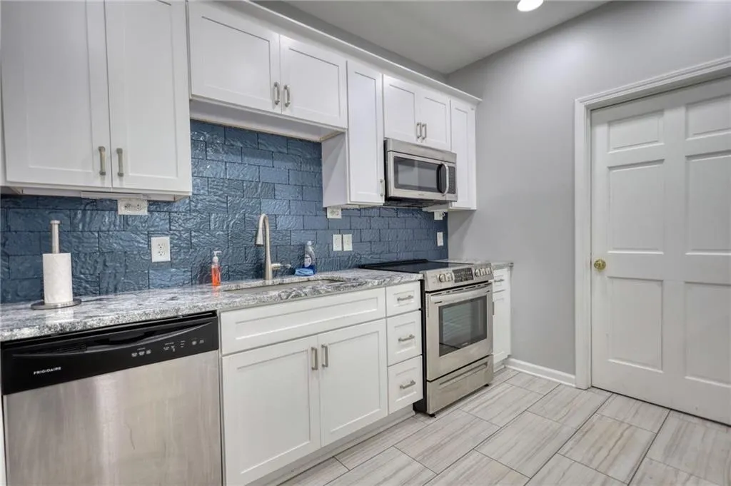 Kitchen featuring stainless steel appliances, white cabinetry, backsplash, light stone counters, and recessed lighting