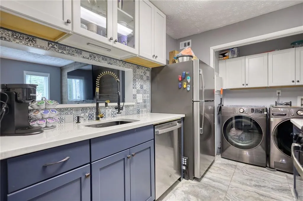Kitchen featuring decorative backsplash, dishwasher, washing machine and dryer, glass insert cabinets, and white cabinets