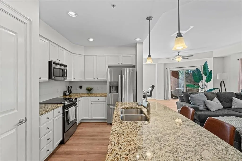 Kitchen with light stone countertops, sink, stainless steel appliances, decorative light fixtures, and white cabinets