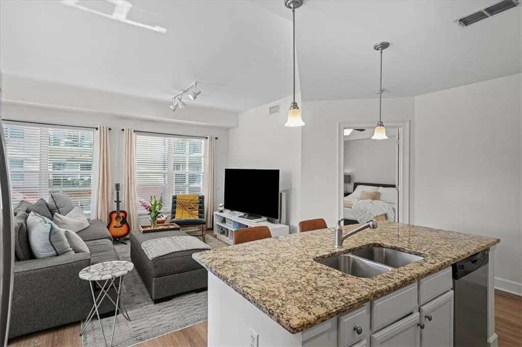 Kitchen with light stone counters, sink, decorative light fixtures, a center island with sink, and dishwasher