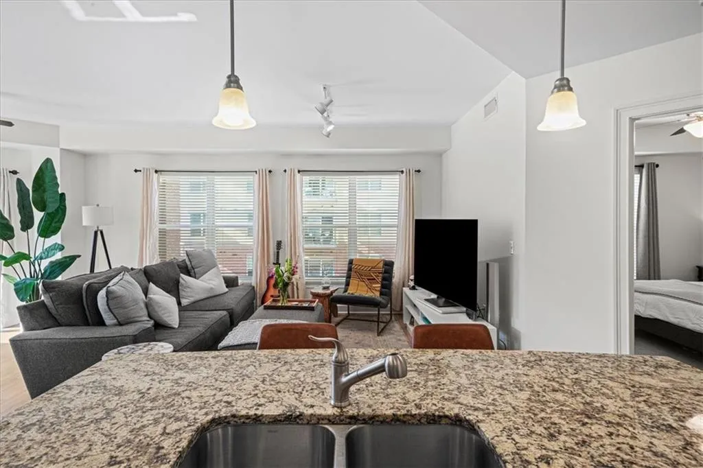 Kitchen featuring rail lighting, light stone counters, hanging light fixtures, and sink