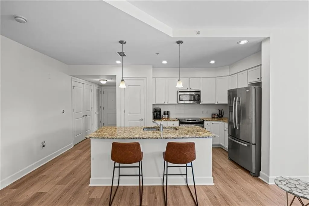 Kitchen featuring white cabinetry, an island with sink, light stone counters, and appliances with stainless steel finishes