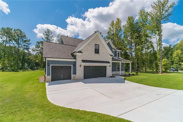Light-colored brick exterior with dark trim accents, featuring a covered front porch and a two-car garage with dark paneled doors