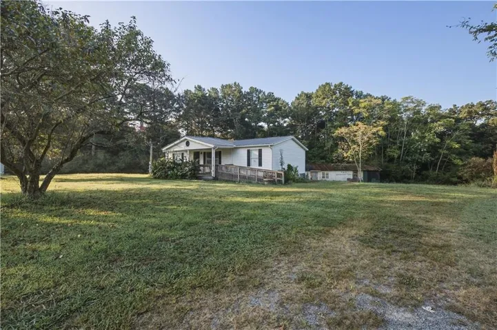 Expansive front yard with mature trees, a covered porch, and a dedicated access ramp