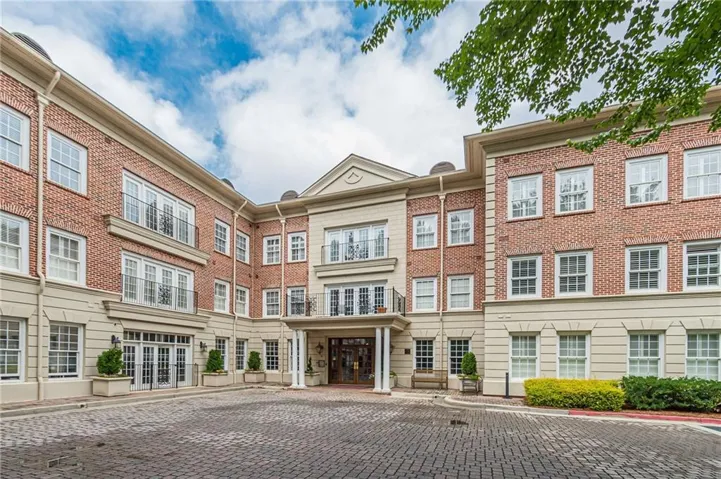 Brick exterior with stone accents, multiple balconies with iron railings, covered entry, and a paver drive