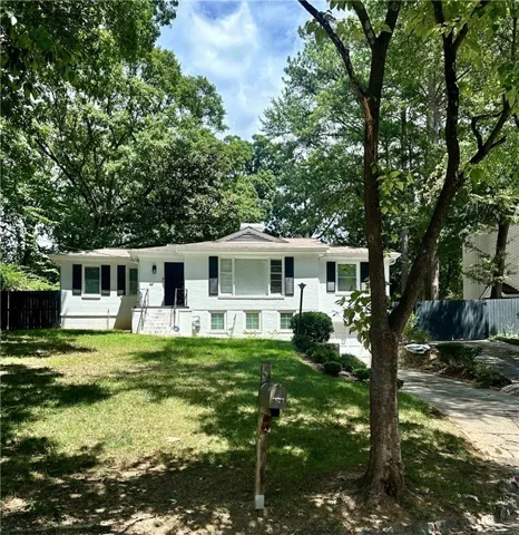 White brick exterior with dark shutters, front entry with steps and handrails, an established front lawn, mature perimeter trees, and a paved driveway