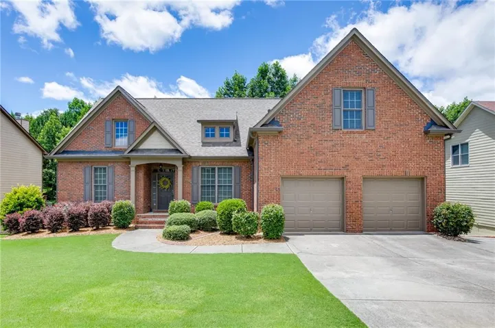 Brick facade residence featuring a covered entry, gabled rooflines, a two-car garage, and established landscaping