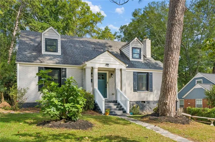 Brick exterior with a dormer window, black window shutters, a teal front door, and a stone walkway