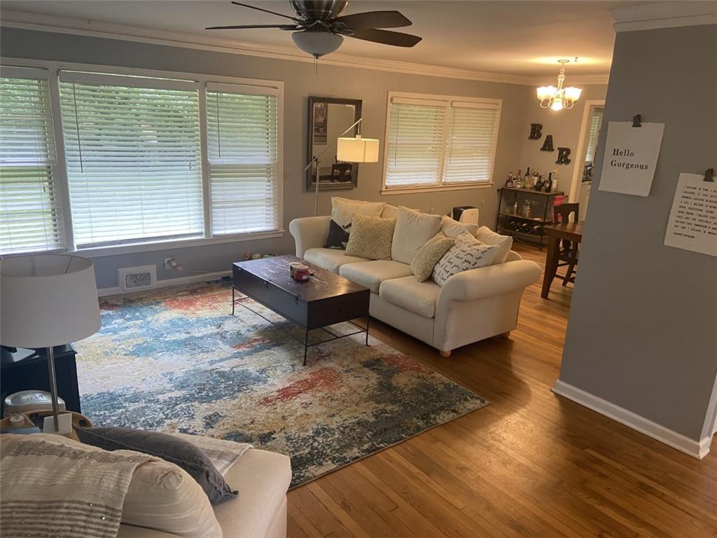 Living room with wood-type flooring, ceiling fan with notable chandelier, and ornamental molding