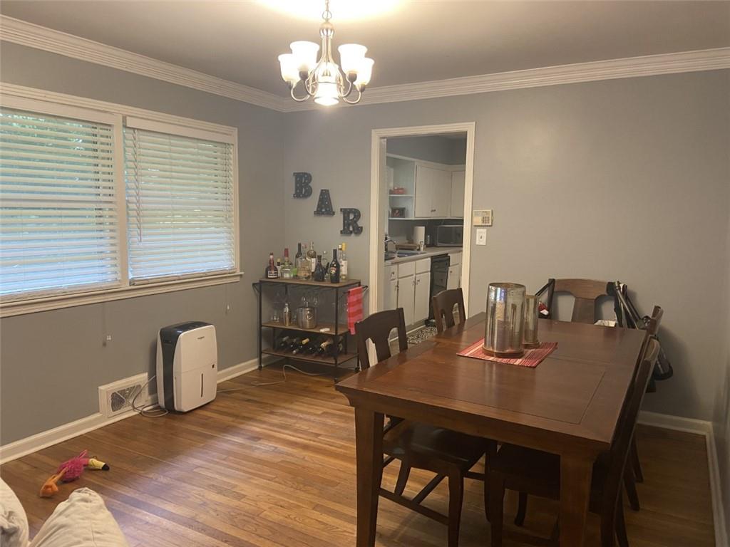 Dining space featuring wood-type flooring, crown molding, and a notable chandelier