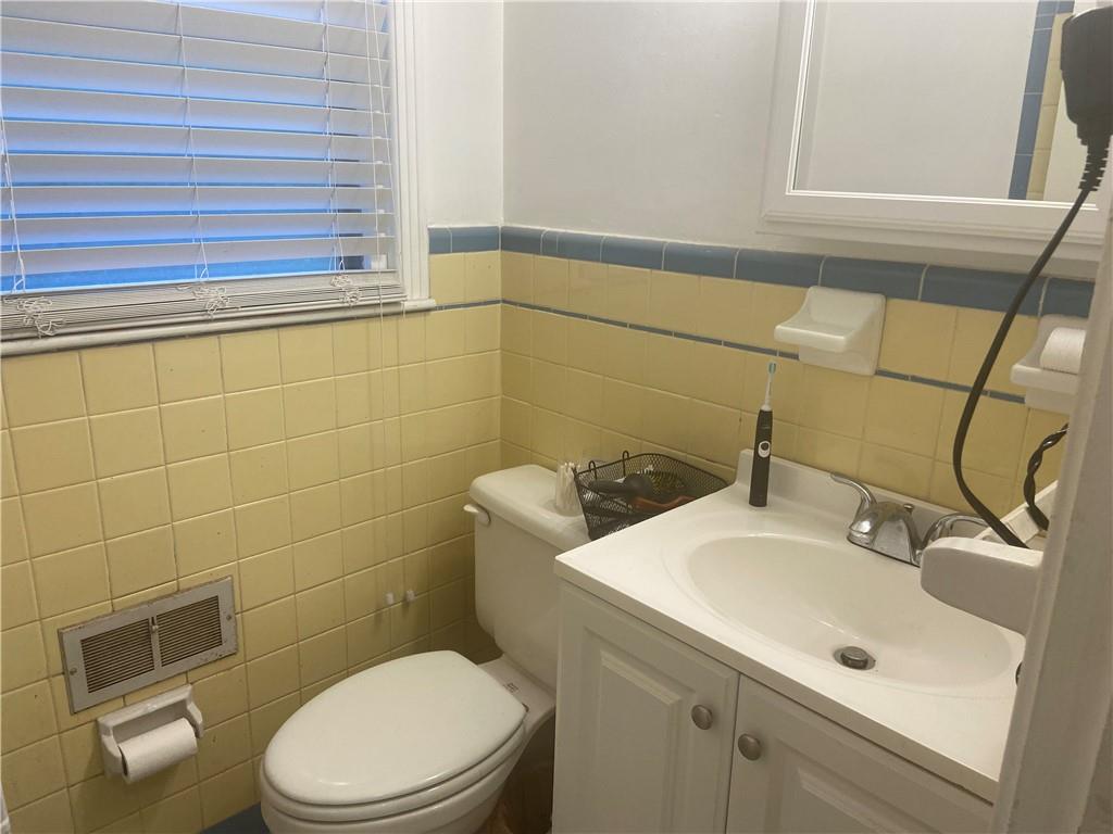 Bathroom featuring toilet, large vanity, tile walls, and backsplash