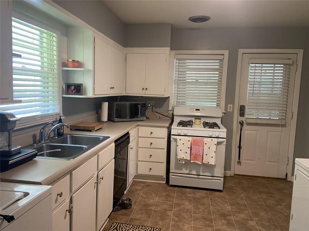 Kitchen with black dishwasher, white cabinets, sink, white range with gas cooktop, and dark tile flooring