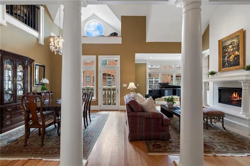 Living area with wood finished floors, a high ceiling, a warm lit fireplace, and decorative columns