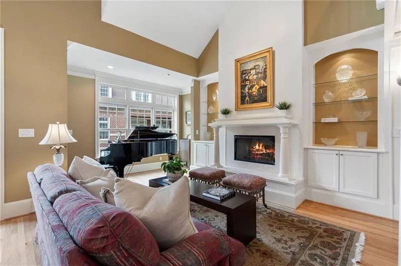 Living room featuring light wood finished floors, a warm lit fireplace, built in shelves, high vaulted ceiling, and baseboards