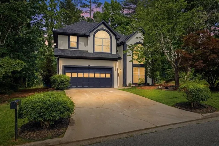 Stucco exterior with dark trim accents, featuring a two-car garage with a paneled door