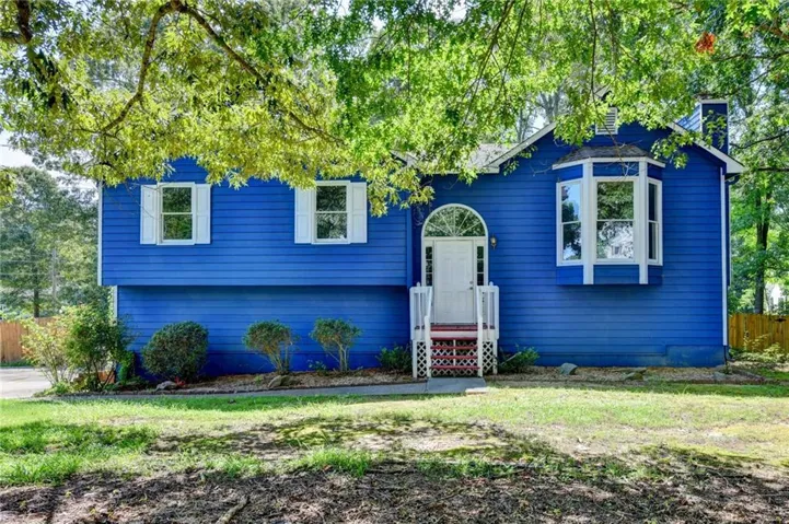Exterior featuring blue siding, white window shutters, an arched entryway, a bay window, and a white front door with a small porch