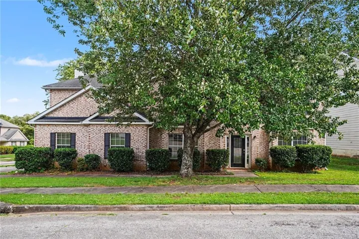Brick exterior featuring a gabled roofline, multiple windows with dark shutters, and mature landscaping