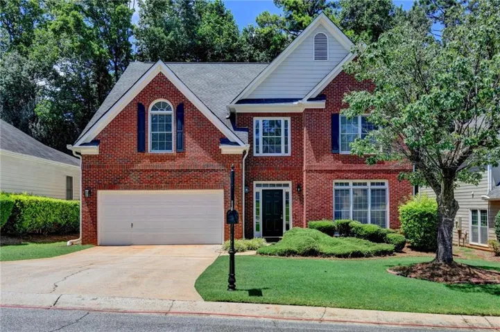 Traditional brick-front residence featuring a two-car garage, established front landscaping, arched and rectangular windows with shutters, and a prominent front entry
