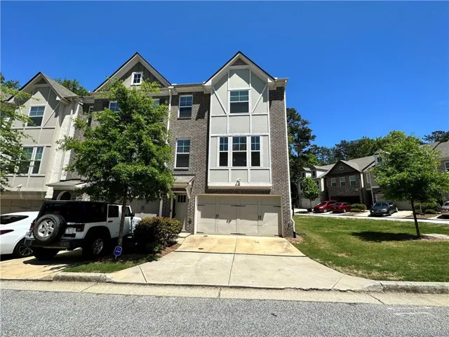 Three-story townhome with a brick and siding exterior, multi-pane windows, and an integrated two-car garage