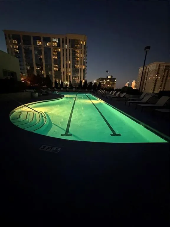 Pool at night with a community pool, a view of city lights, and a patio area Pool at night with a community pool, a view of city lights, and a patio area