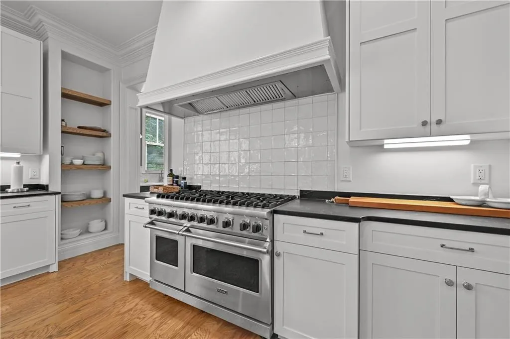 Kitchen with custom range hood, double oven range, open shelves, dark countertops, and ornamental molding