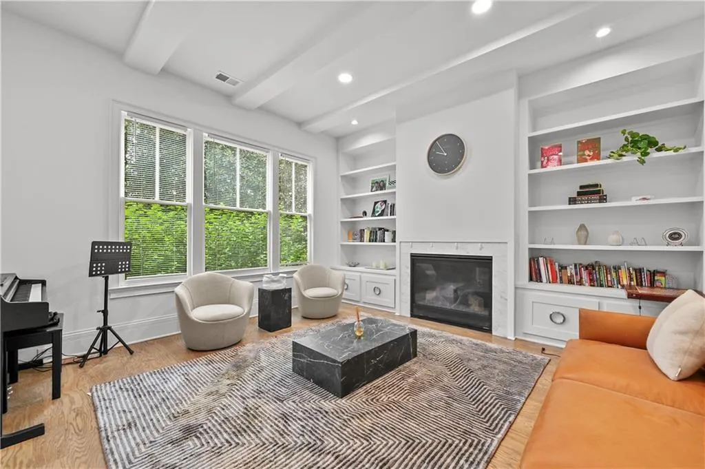 Living room featuring built in features, a premium fireplace, beam ceiling, light wood-style flooring, and recessed lighting