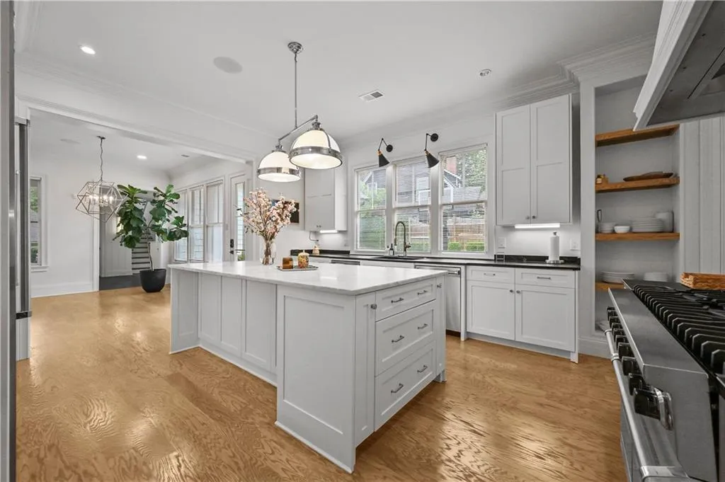 Kitchen with light wood-type flooring, ventilation hood, ornamental molding, a kitchen island, and white cabinets