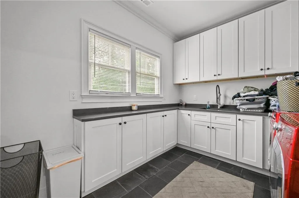 Kitchen with crown molding, dark countertops, washer and clothes dryer, white cabinetry, and dark tile patterned flooring