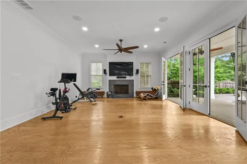 Workout area with french doors, ornamental molding, wood finished floors, a fireplace, and ceiling fan
