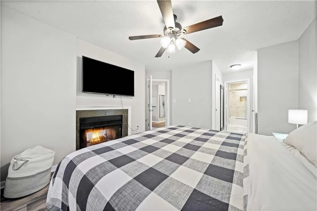 Bedroom featuring ceiling fan, ensuite bath, a fireplace, and a textured ceiling