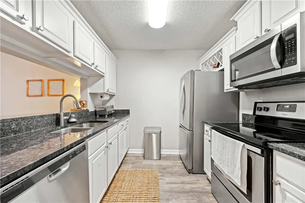 Kitchen featuring stainless steel appliances, sink, dark stone countertops, and white cabinets