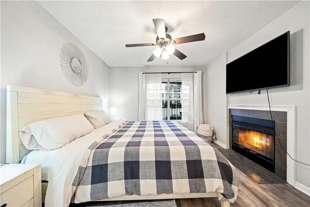 Bedroom with a tile fireplace, dark wood-type flooring, ceiling fan, and a textured ceiling