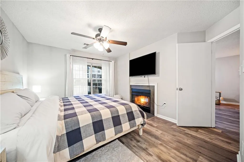Bedroom with a tiled fireplace, ceiling fan, hardwood / wood-style floors, and a textured ceiling