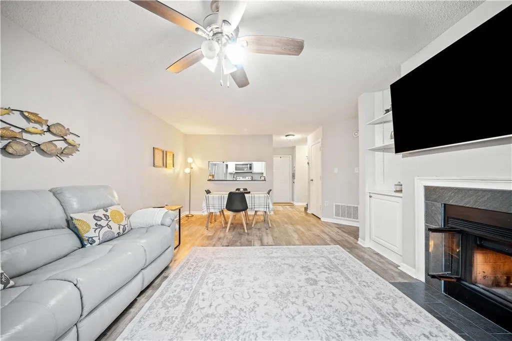 Living room with ceiling fan, wood-type flooring, a tiled fireplace, and a textured ceiling