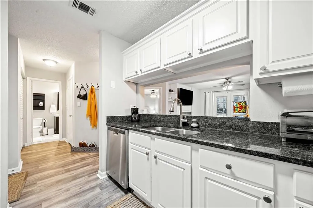 Kitchen featuring white cabinetry, sink, stainless steel dishwasher, ceiling fan, and a textured ceiling