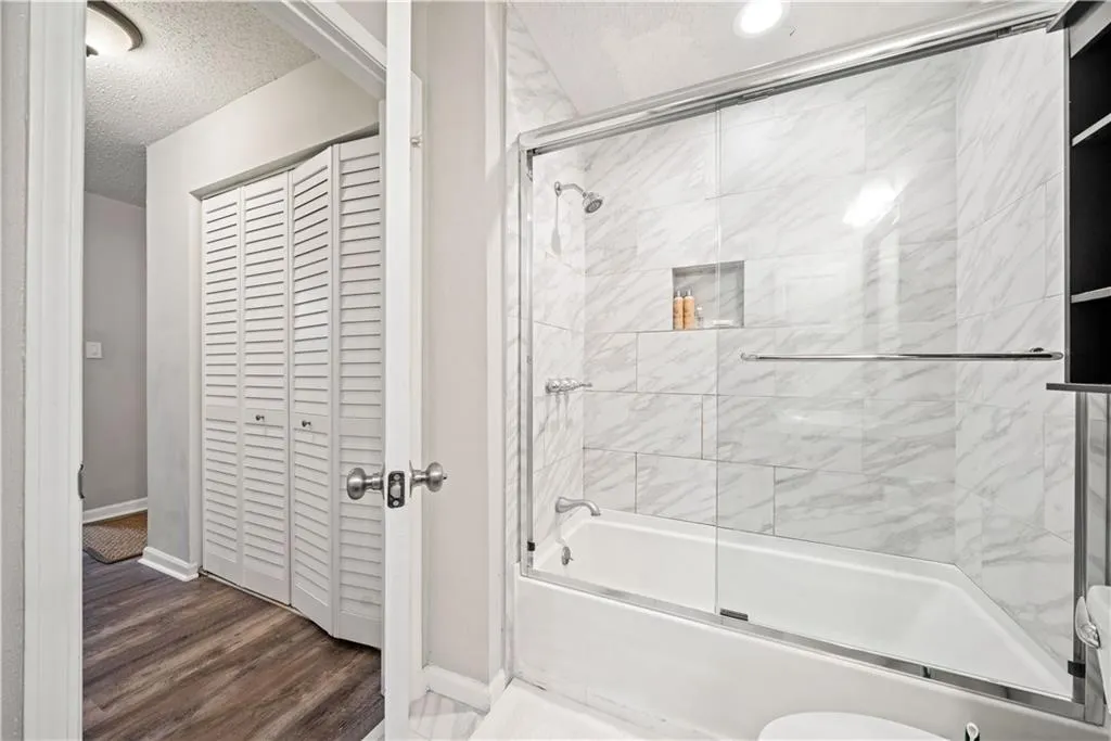 Bathroom with hardwood / wood-style flooring, bath / shower combo with glass door, toilet, and a textured ceiling