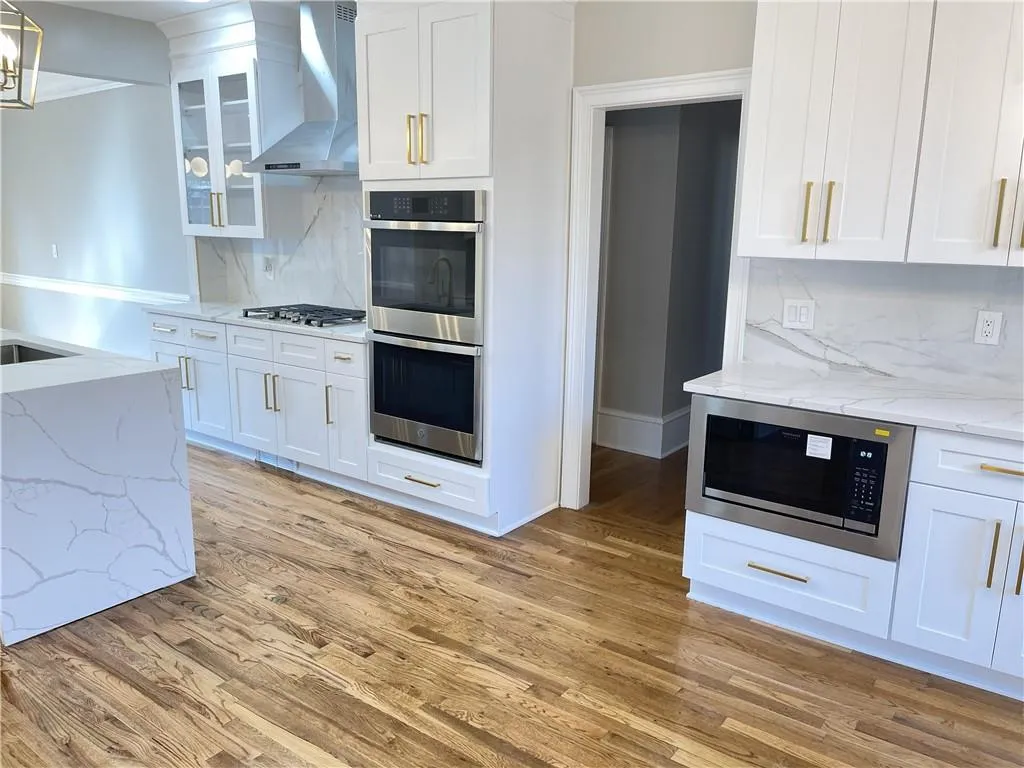 Kitchen with decorative backsplash, light stone counters, stainless steel appliances, and white cabinets