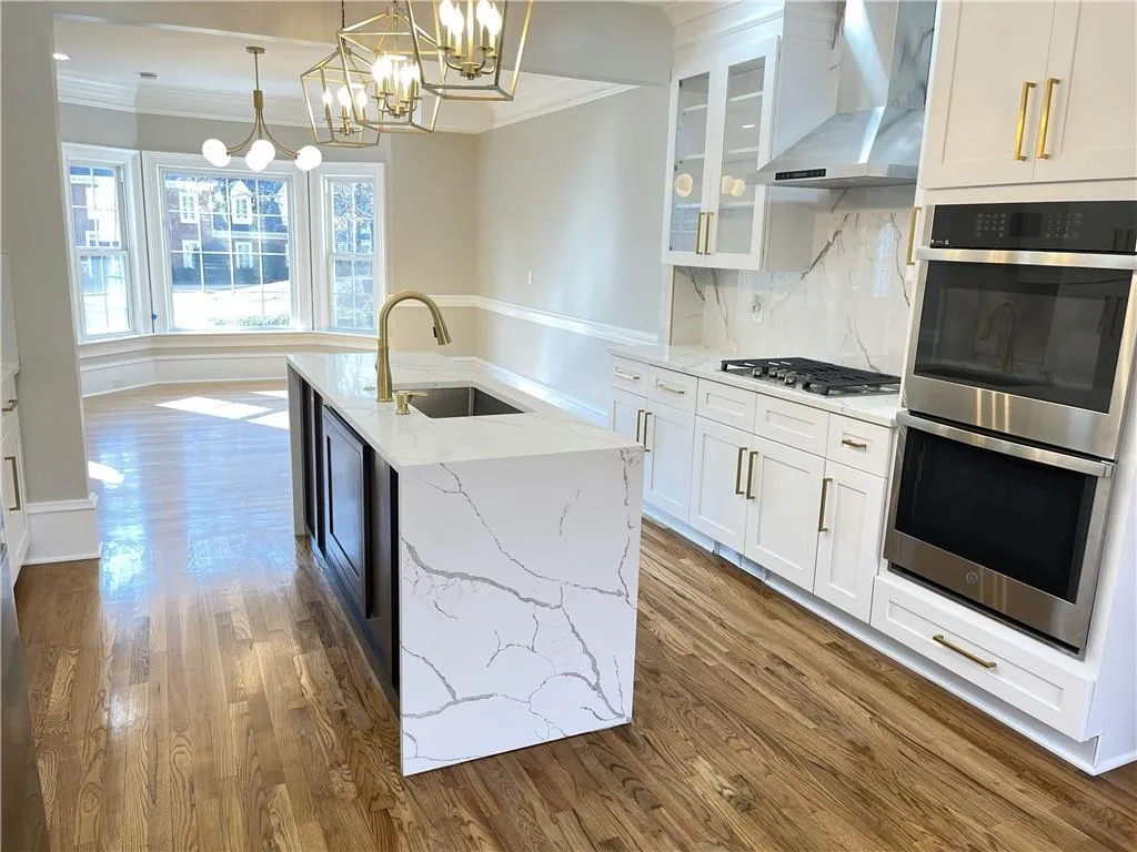 Kitchen featuring stainless steel appliances, hanging light fixtures, wall chimney exhaust hood, light stone counters, and ornamental molding
