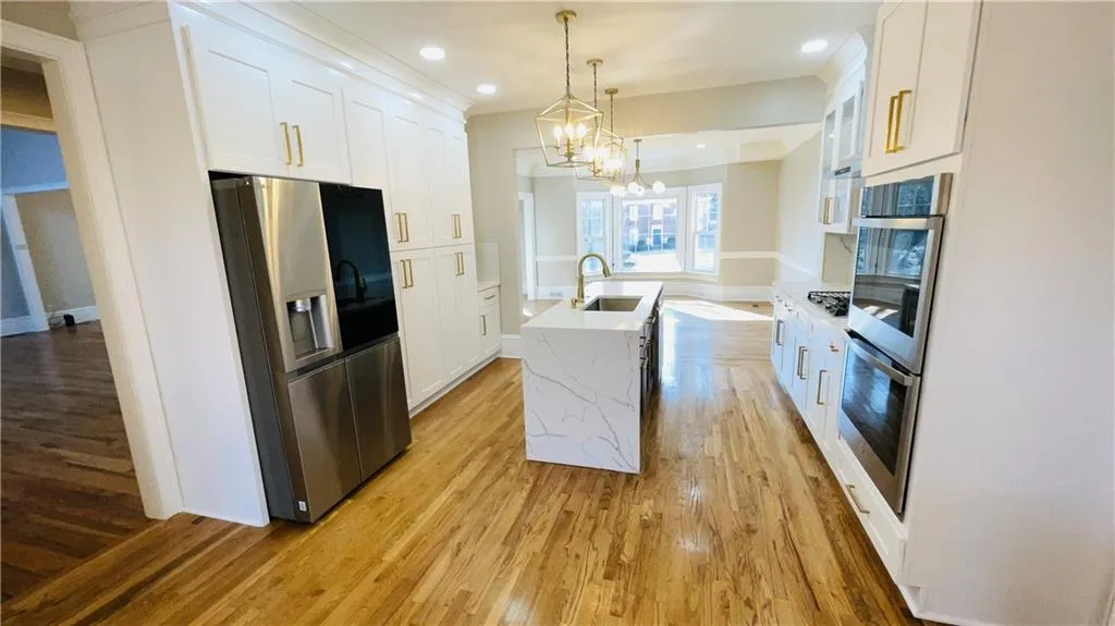 Kitchen featuring appliances with stainless steel finishes, a kitchen island with sink, decorative light fixtures, light wood-style flooring, and white cabinets