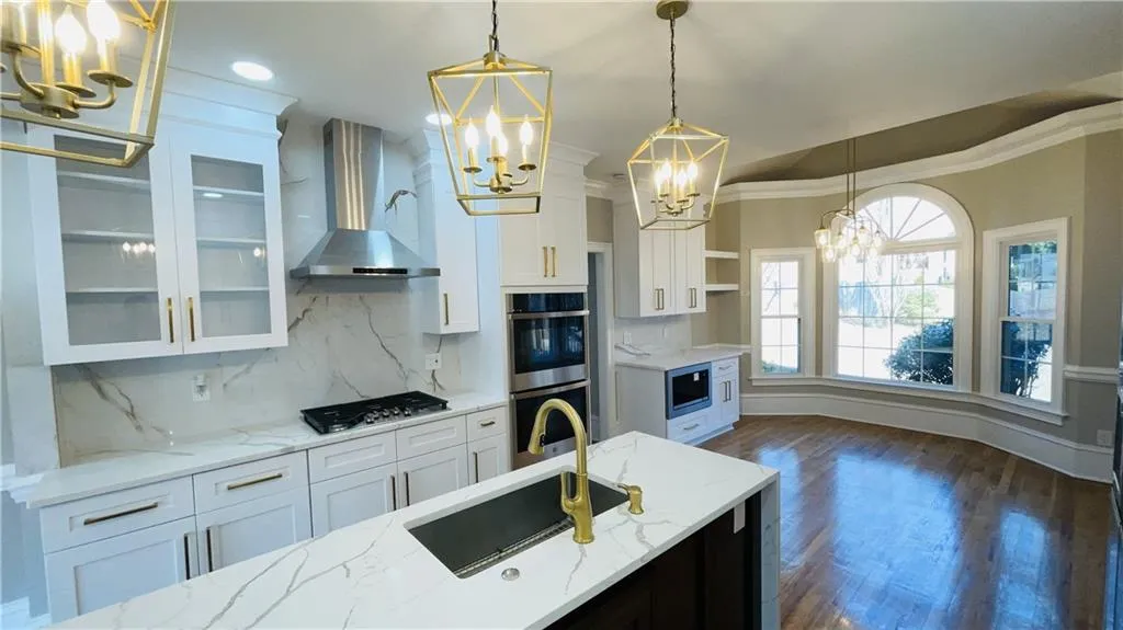 Kitchen with a chandelier, pendant lighting, white cabinetry, wall chimney range hood, and glass insert cabinets