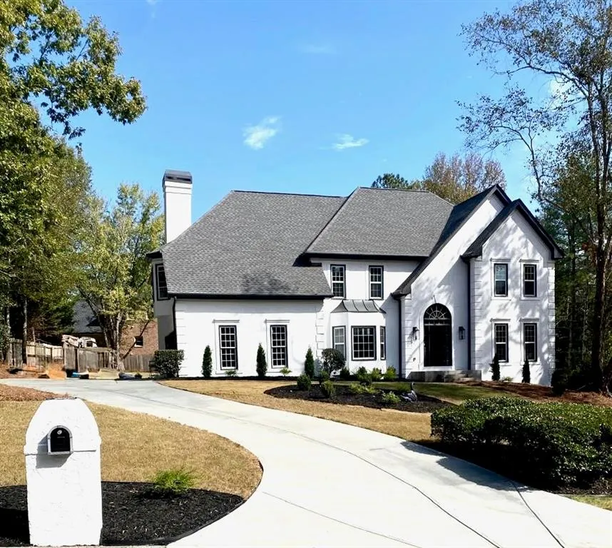 View of front of home featuring a shingled roof, a chimney, curved driveway, and stucco siding
