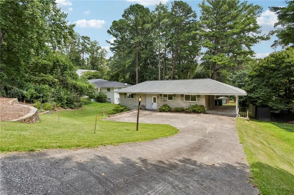 View of front of house with a front yard, driveway, stone siding, view of scattered trees, and a carport