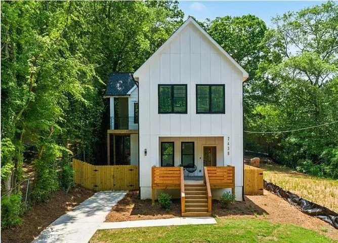 Contemporary farmhouse exterior featuring white board and batten siding, black-framed windows, a wood front porch, and a second-story balcony