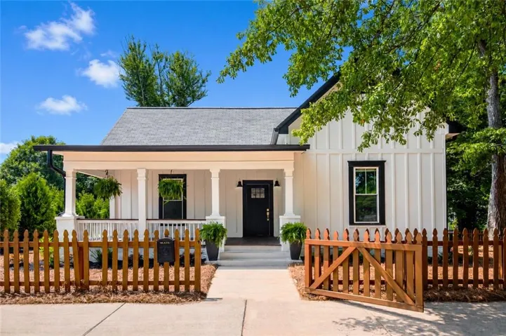 Board and batten exterior with contrasting trim, covered front porch, asphalt shingle roof, and a wood picket fence